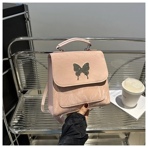 Close-up of pink textured backpack with silver butterfly charm and pleated leather detail