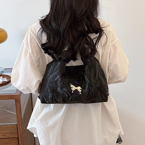 Chic black pleated tote bag with silver bow detail shown in a stylish shoulder carrying view