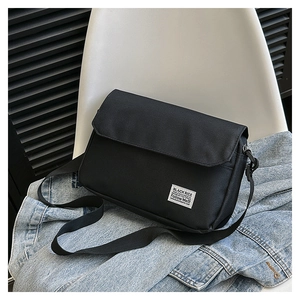 Close-up of black canvas messenger bag with flap closure and white woven brand label