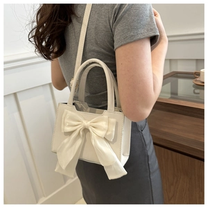 Close-up of cream crossbody bag with large silk bow shown on shoulder by model
