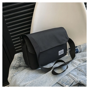 Detail of a black canvas messenger bag with a square white label on light denim jacket