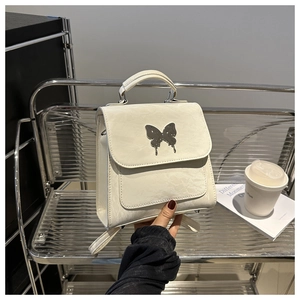 Detail of warm white backpack with wrinkled leather texture and silver butterfly accent