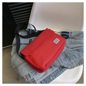 Detail view of a red canvas messenger bag with a black strap and stylish brand label