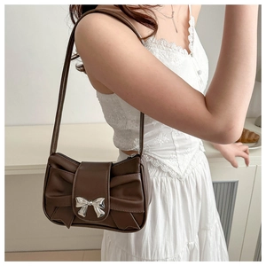 Detailed view of dark brown pleated bag with silver bow buckle on white lace outfit