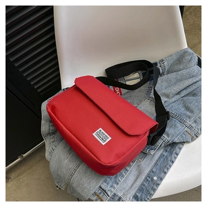 Detail view of red canvas messenger bag placed on denim jacket atop a white chair