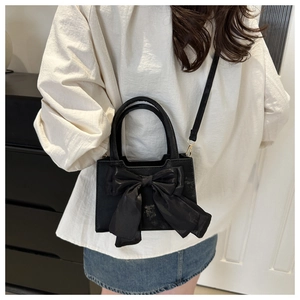 Detailansicht der schwarzen Umhängetasche mit großer Satin-Schleife und goldener Hardware