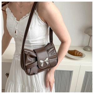 Detail of a dark brown pleated leather shoulder bag with a silver bow buckle on model
