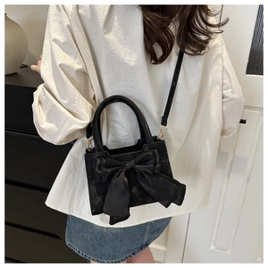 Detail view of a black matte leather handbag with a large silk bow and slender strap