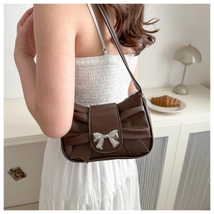 Detail of dark brown shoulder bag with silver bow ornament and elegant pleated design