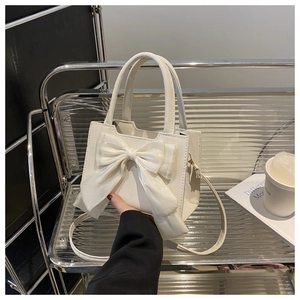 Detail of white square handbag featuring a large decorative bow and elegant dual handles