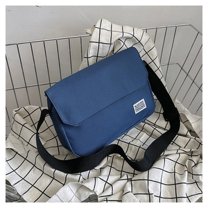 Detail of blue canvas messenger bag with brand logo label and wide black strap