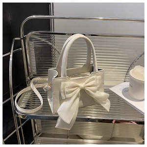 Detail of white structural handbag with a large silk bow and adjustable shoulder strap