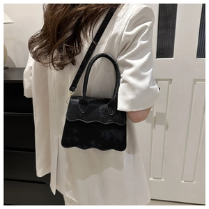Modern black crossbody bag with wave-edge flap shown on model in a stylish home setting
