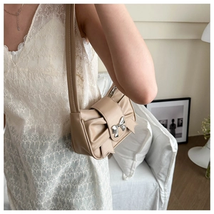 Detail of beige pleated bow shoulder bag with silver metallic clasp on a white dress