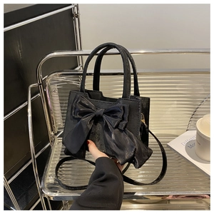 Detail of black bow handbag on silver metal shelf with lifestyle props in minimalist setting