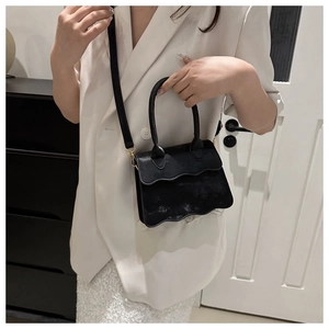 Detail of black crossbody bag featuring unique wavy flap design and gold hardware accents