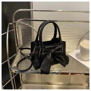 Detail of black bow handbag on metal shelf featuring velvet texture and satin ribbon bow