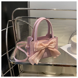 Detail view of pink bow-knot handbag on a stylish stand with lifestyle props