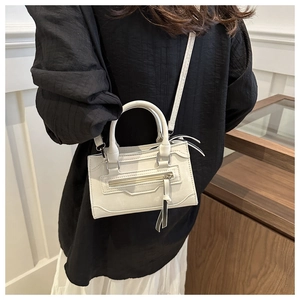 Détail du sac bandoulière crème avec finition mate et glands décoratifs en cuir