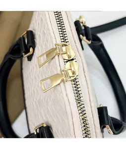 Détail d'un sac à main beige tressé avec double fermeture éclair dorée et anses noires