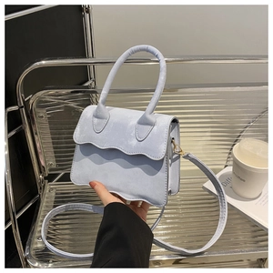 Detail of light blue crossbody bag with wavy flap design and circular handle grip
