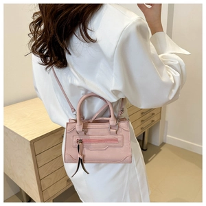 Détail du mini sac à main rose style motard porté par un mannequin dans une pièce