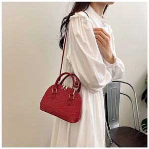 Détail du sac bandoulière rouge en forme de coquillage avec texture tressée et métal doré