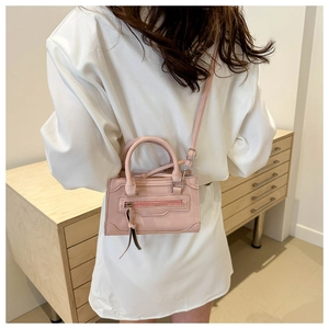 Détail du mini sac rose à pompons porté par un mannequin en robe blanche élégante