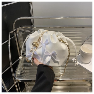 Détail du sac seau blanc avec des nœuds en satin et une bandoulière dorée