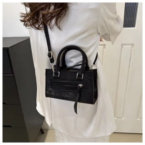 Détail d'un sac à bandoulière noir avec boucles argentées porté sur une chemise blanche