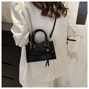 Détail d'un sac à bandoulière noir avec texture vintage et long gland sur satin blanc