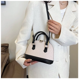Détail du sac coquillage beige et noir à texture tissée porté par un mannequin en blazer