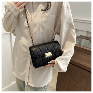 Detail of black quilted crossbody bag with metal lock and chain strap on model