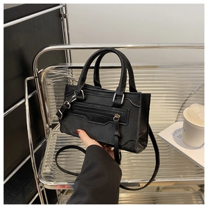 Détail d'un sac à main en cuir noir mat avec glands décoratifs et doubles poignées