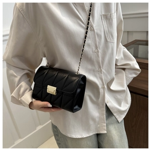 Detail of black quilted crossbody bag featuring a gold metal clasp and chain strap