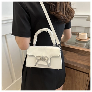 Detail der weißen Ledertasche mit glitzernder Kristallschleife und Cloud-Faltengriff