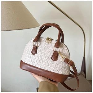 Détail du sac coquillage montrant la texture tissée, le cuir brun et le métal doré