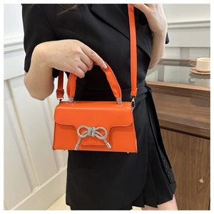 Detail der orangefarbenen Kunstleder-Handtasche mit funkelnder Strass-Schleife und Kette