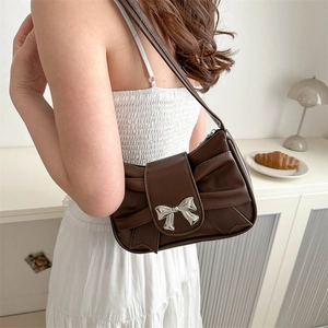 Dark brown pleated bow shoulder bag with silver metal buckle shown in a lifestyle setting