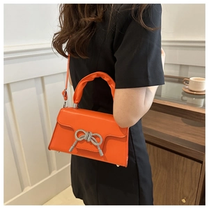 Detail der orangefarbenen Handtasche mit glitzernder Strass-Schleife und gerafftem Griff