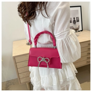 Detail der rosafarbenen Handtasche mit glitzernder Schleife und Faltenhebel am Modell