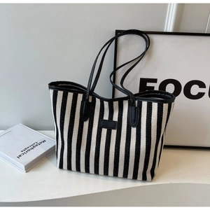 Close-up of black and white striped tote bag with leather handles and central logo patch