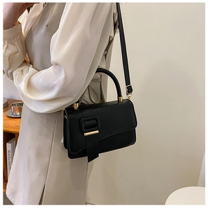 Detailed view of black leather crossbody bag with gold buckle on a minimalist outfit