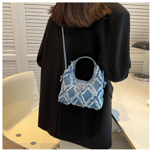 Détail macro du sac seau en denim bleu avec surpiqûres effilochées et fermoir rotatif