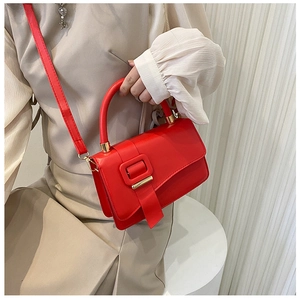Detail of bright red faux leather crossbody bag with round handle and gold hardware accent