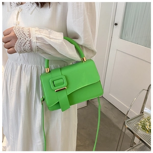 Close-up of bright green small square bag with textured leather buckle on a white dress