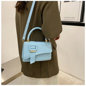Detail of baby blue leather shoulder bag with square buckle on green blazer background