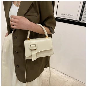 Detail of off-white top handle bag with olive green suit and gold metal hardware accents
