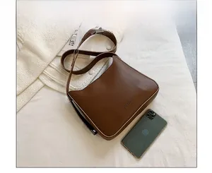 Detailed size comparison of deep brown leather shoulder bag with a smartphone and magazine
