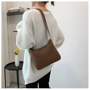 Brown matte leather shoulder bag detail with shoulder strap worn over cream knit sweater
